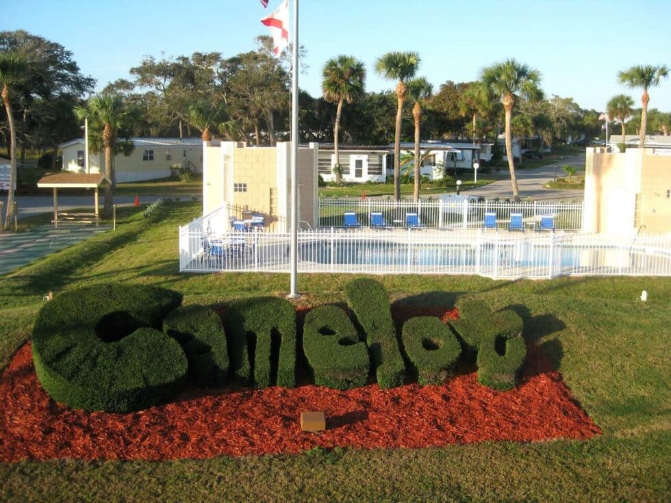 Green topiary bushes shaped into the word “Camelot” in front of the community pool and facilities at Camelot RV Park in Malabar, Florida