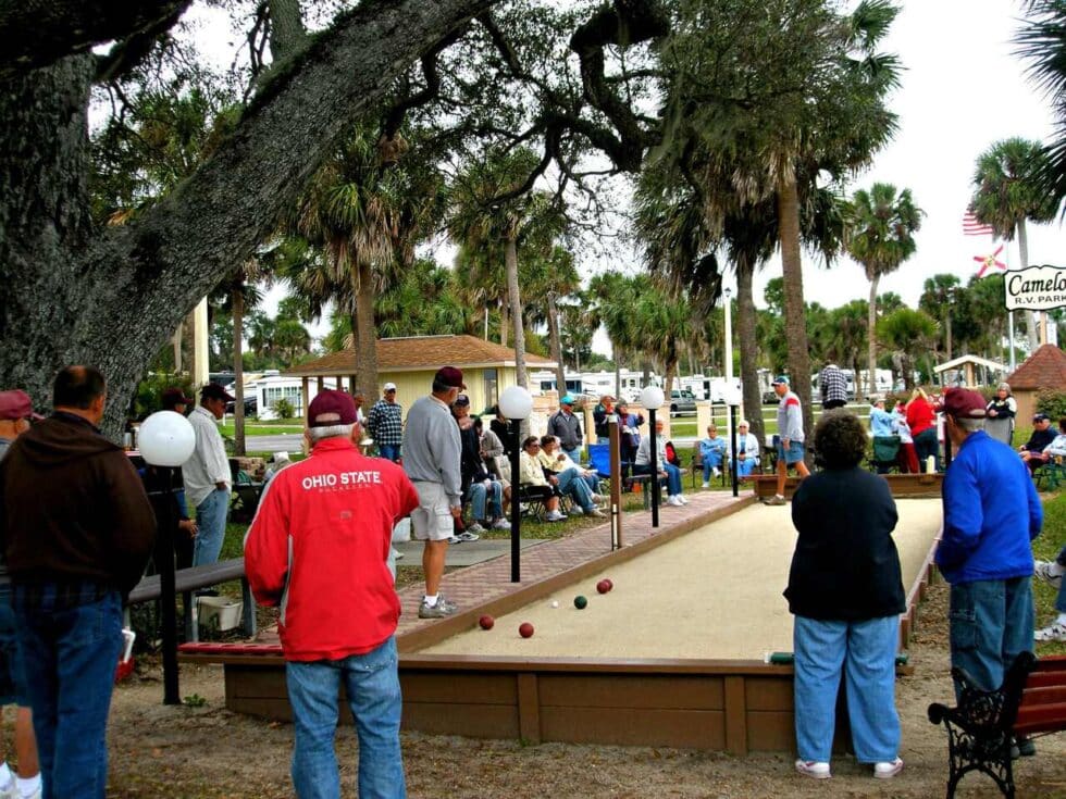 Group of residents playing bocce ball and socializing under large trees at Camelot RV Park