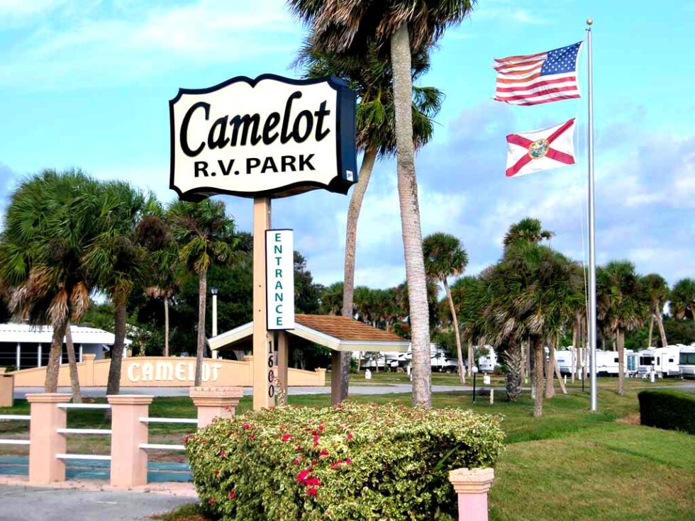 Entrance sign at Camelot RV Park in Malabar, Florida with American and Florida flags waving in the background