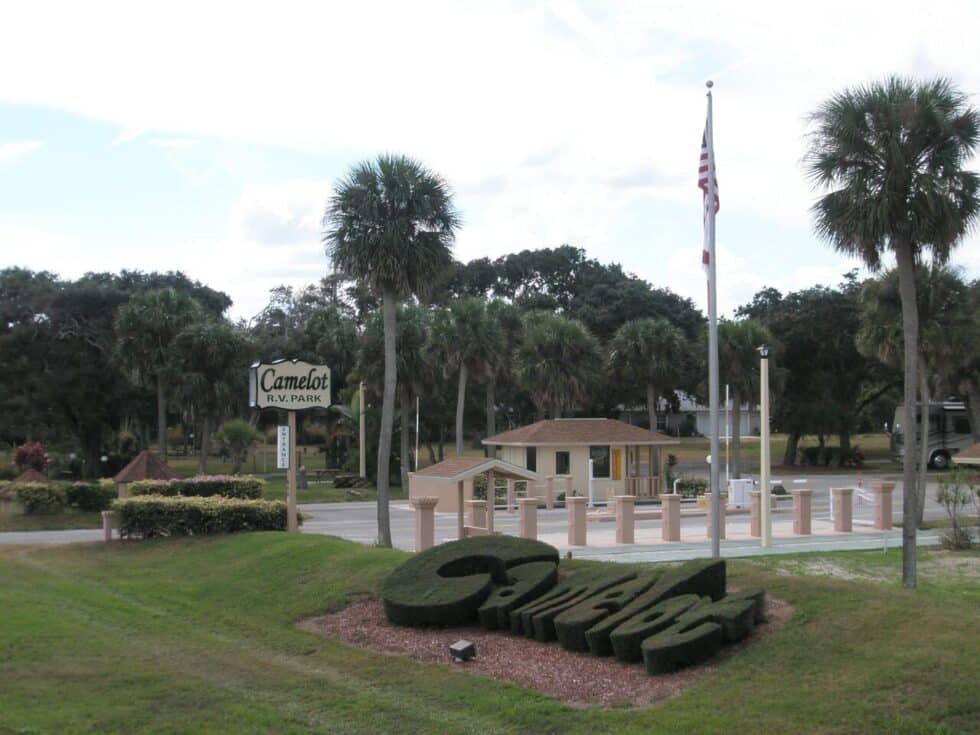 Gated front entrance with palm trees and a welcoming Camelot RV Park sign in Malabar, Florida