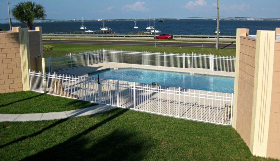 Heated swimming pool with white fence and lounge chairs overlooking the Indian River in Camelot RV Park