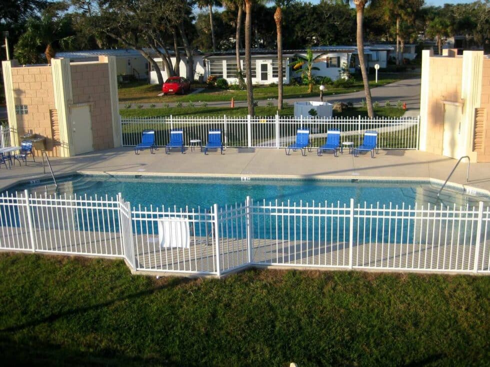 Overview of the fenced heated pool with lounge chairs and palm trees at Camelot RV Park