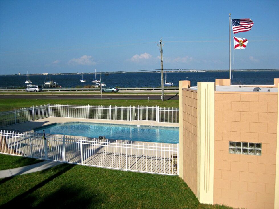 Sparkling pool at Camelot RV Park with American and Florida flags flying, overlooking the Indian River Lagoon