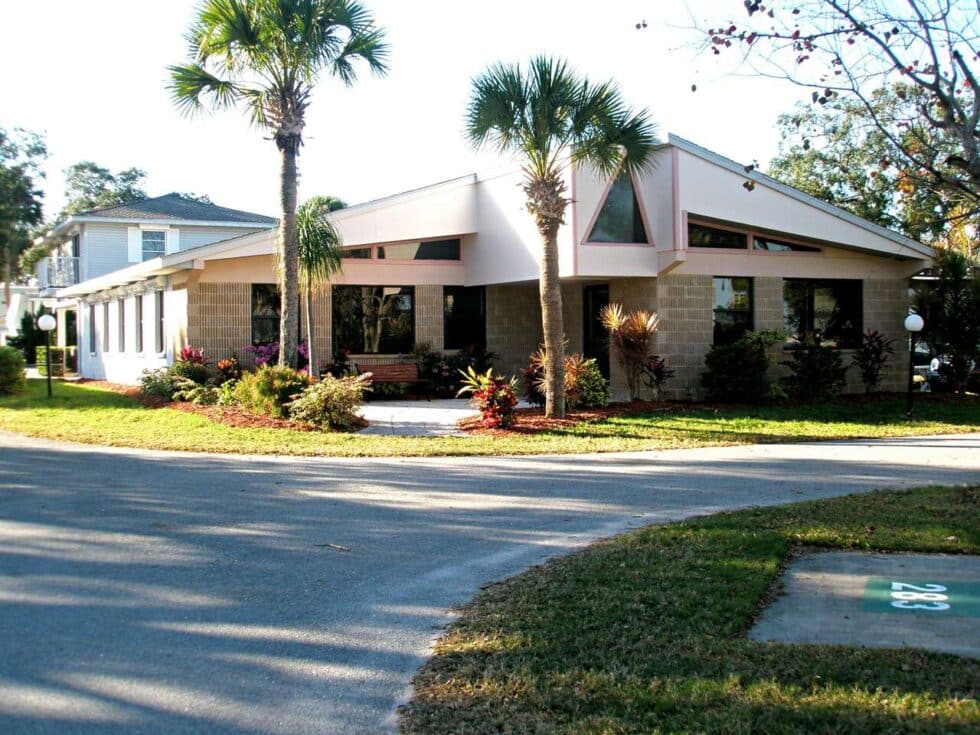 Exterior of the recreation hall at Camelot RV Park surrounded by palm trees and landscaping