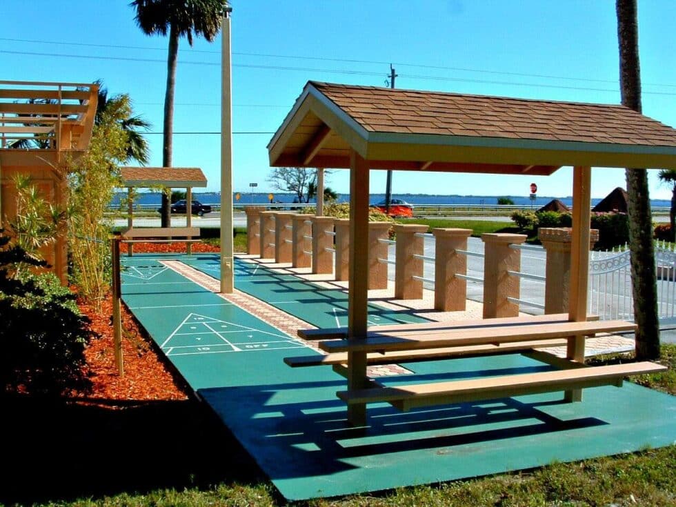 Outdoor shuffleboard courts shaded with wooden structures and a view of the Indian River Lagoon in the background