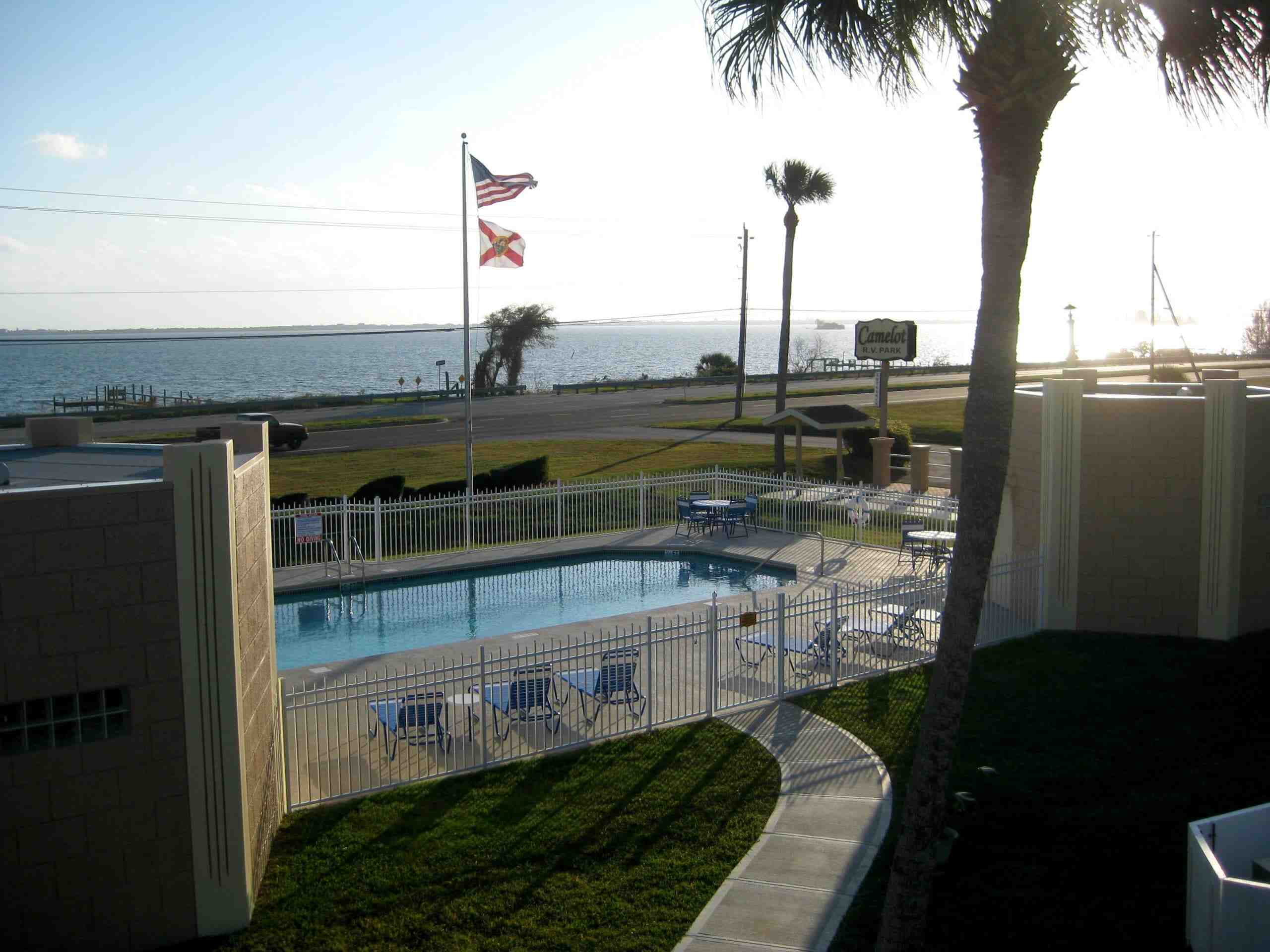 Camelot RV Park’s heated pool with chairs and riverfront view under palm trees